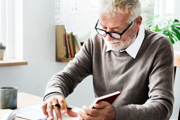 Man with glasses sitting at desk writing in notebook.